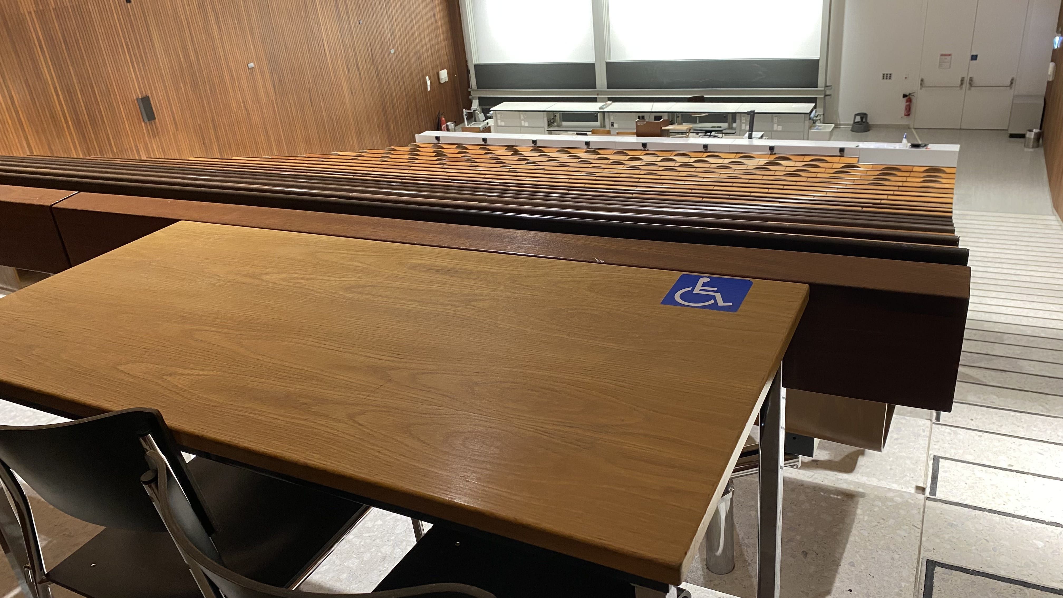 Hörsaal Y15-G-60: Ansicht auf den Tisch mit Rollstuhl-Signet ohne fixe Bestuhlung. Der Tisch befindet sich in der hintersten Reihe unmittelbar vor der rechten Eingangstür.