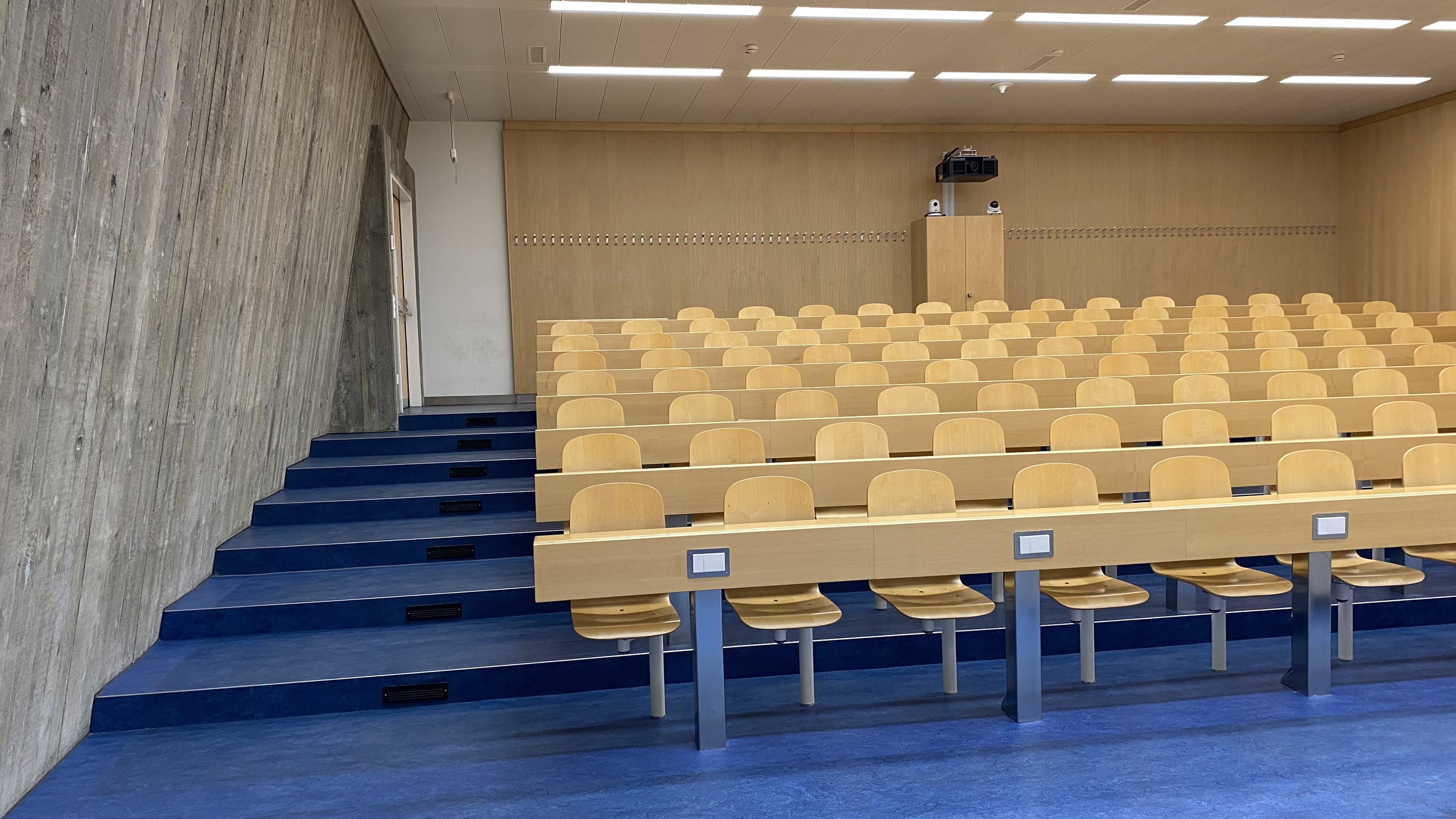 Seminarraum Y35-F-32: Ansicht auf den Raum von der ersten Eingangstür aus. Stufen führen links zur oberen Sitzreihe. Die oberste Sitzreihe kann durch eine zweite, stufenlose Eingangstür erreicht werden.