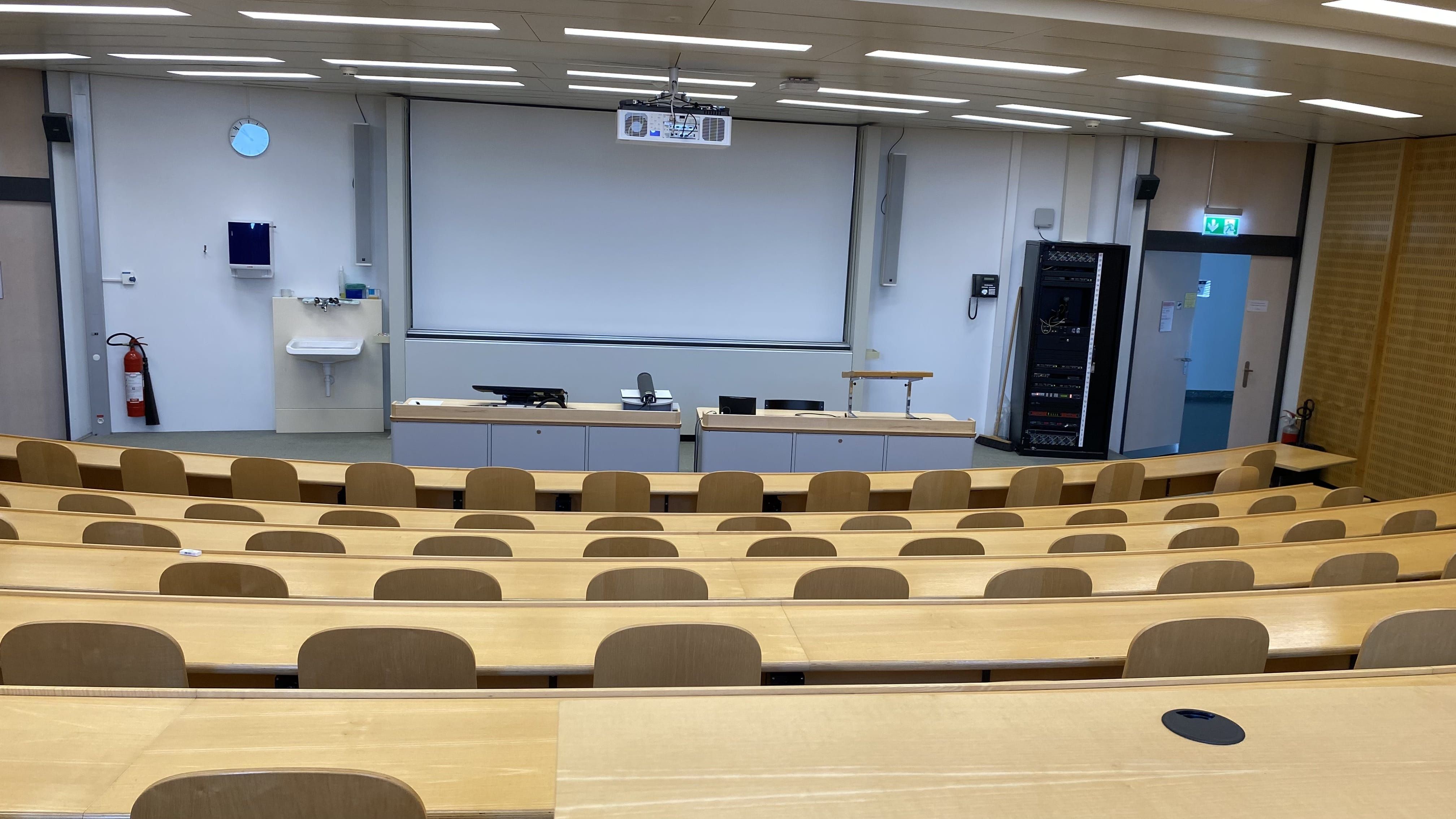 Hörsaal Y17-M-05: Ansicht auf den Raum von der hintersten Reihe aus. Links und rechts sind die Eingangstüren ersichtlich.