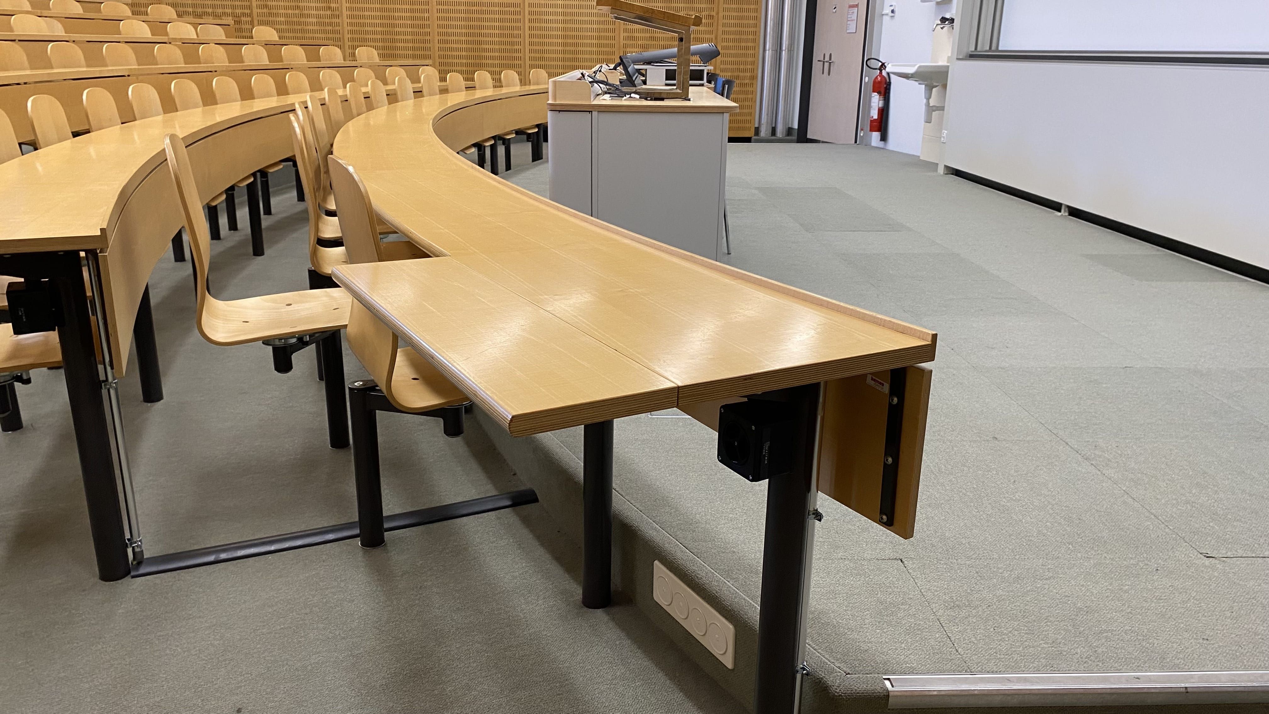 Hörsaal Y17-M-05: Ansicht auf den zweiten von zwei aufklappbaren Tischen ohne fixe Bestuhlung. Dieser Tisch befindet sich in der vordersten Reihe ganz links und ist stufenlos über die linke Eingangstür erreichbar.