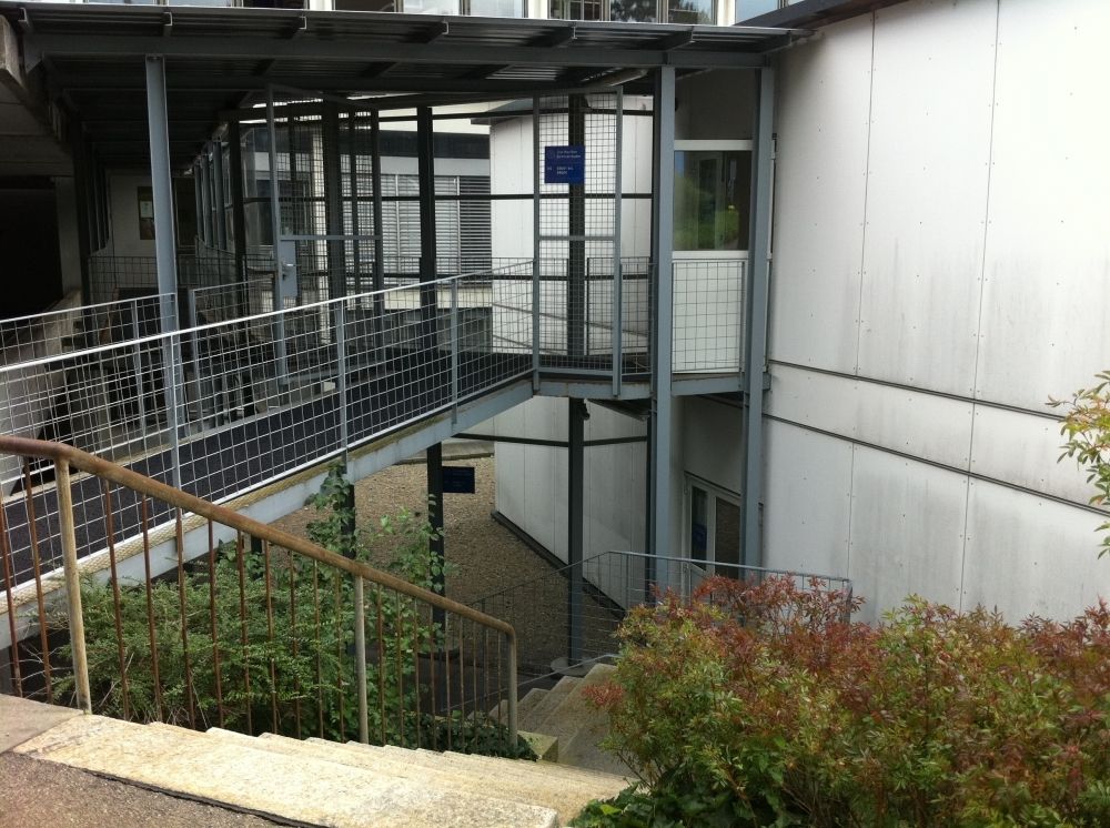Gebäude GLT: Vorne rechts (oben): Eingangstüre ins Stockwerk BB.
Vorne rechts (unten): Eingangstüre ins Stockwerk AA.
Hinten links (oben): Eingangstüre ins Gebäude ZUI, um stufenlos ins Stockwerk AA zu gelangen oder zu den Rollstuhl-Parkplätzen.