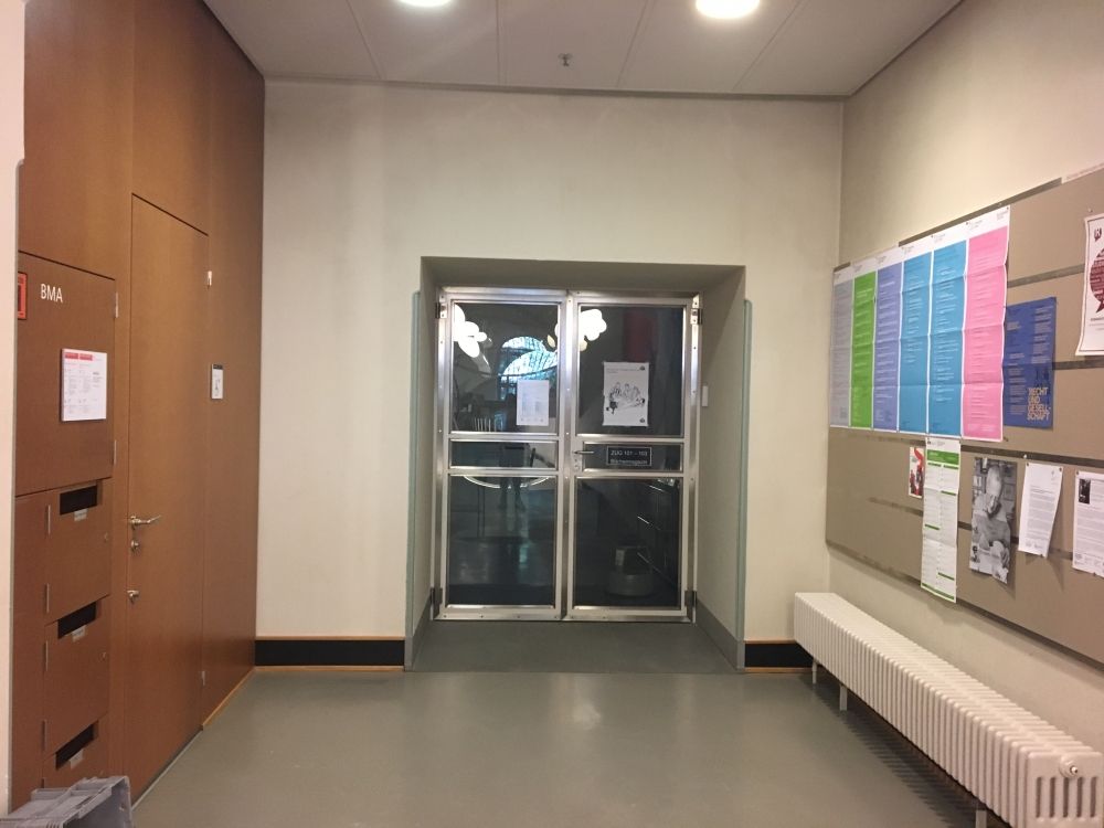 Rollstuhl-WC ZUG-D-71: Blick nach links von der Mitte des Gebäudes im Geschoss D. Die Braune Tür auf der linken Seite im Foto ist das Rollstuhl WC.