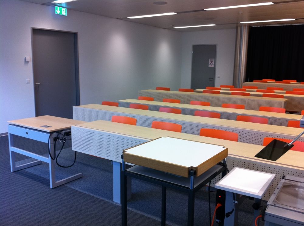 Hörsaal AFL-F-121: (Hinten) links: Eingangstüre in den Hörsaal
(vorne) links: spezieller, elektrisch höhenverstellbarer Tisch.