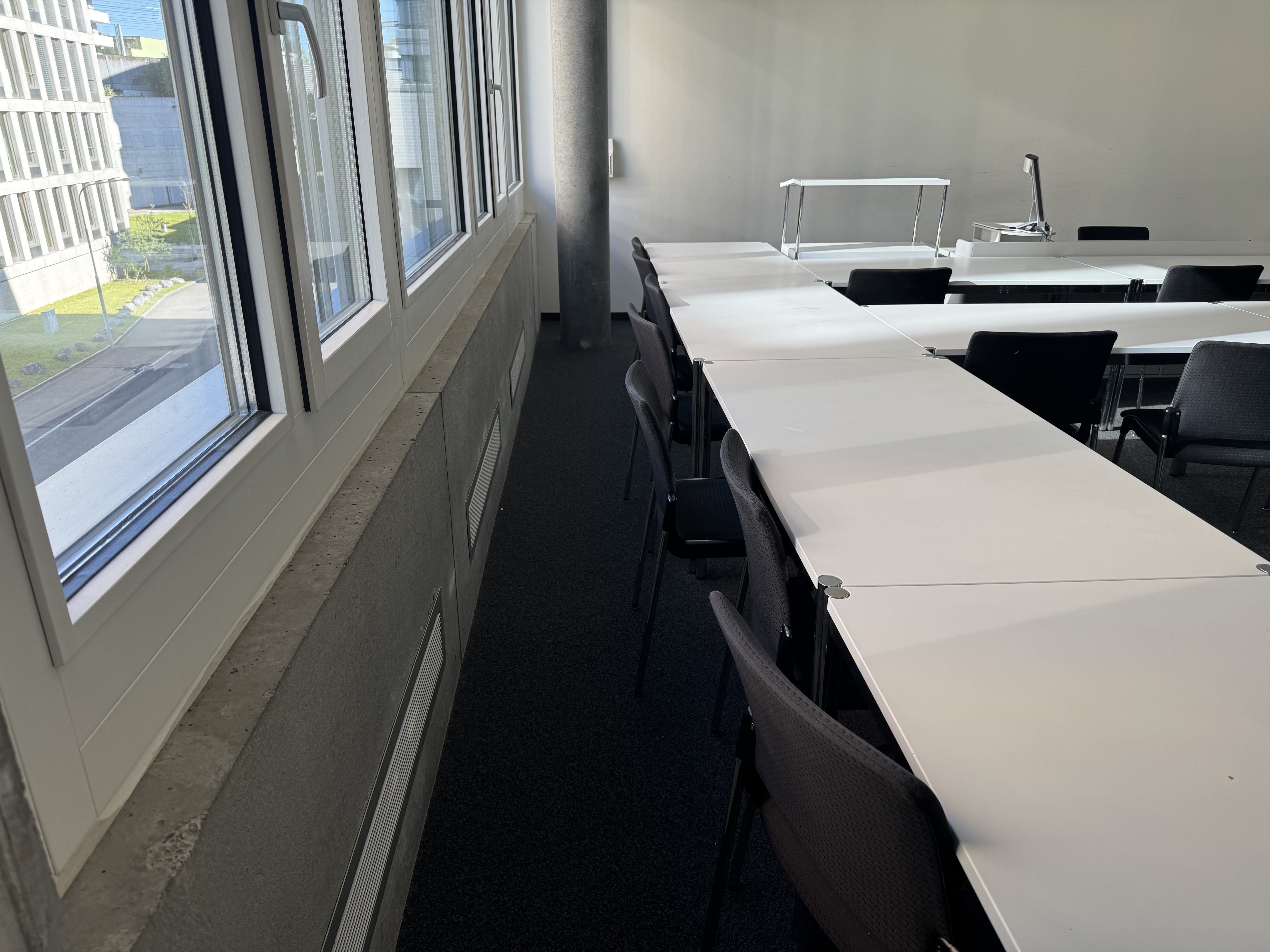 Seminarraum AND-02-02: Ansicht auf die Stuhlreihe auf der linken Seite des Raumes neben den Fenstern. Eine Säule steht im Weg von der linken Seite des Raumes hin zum Dozierendenpult.