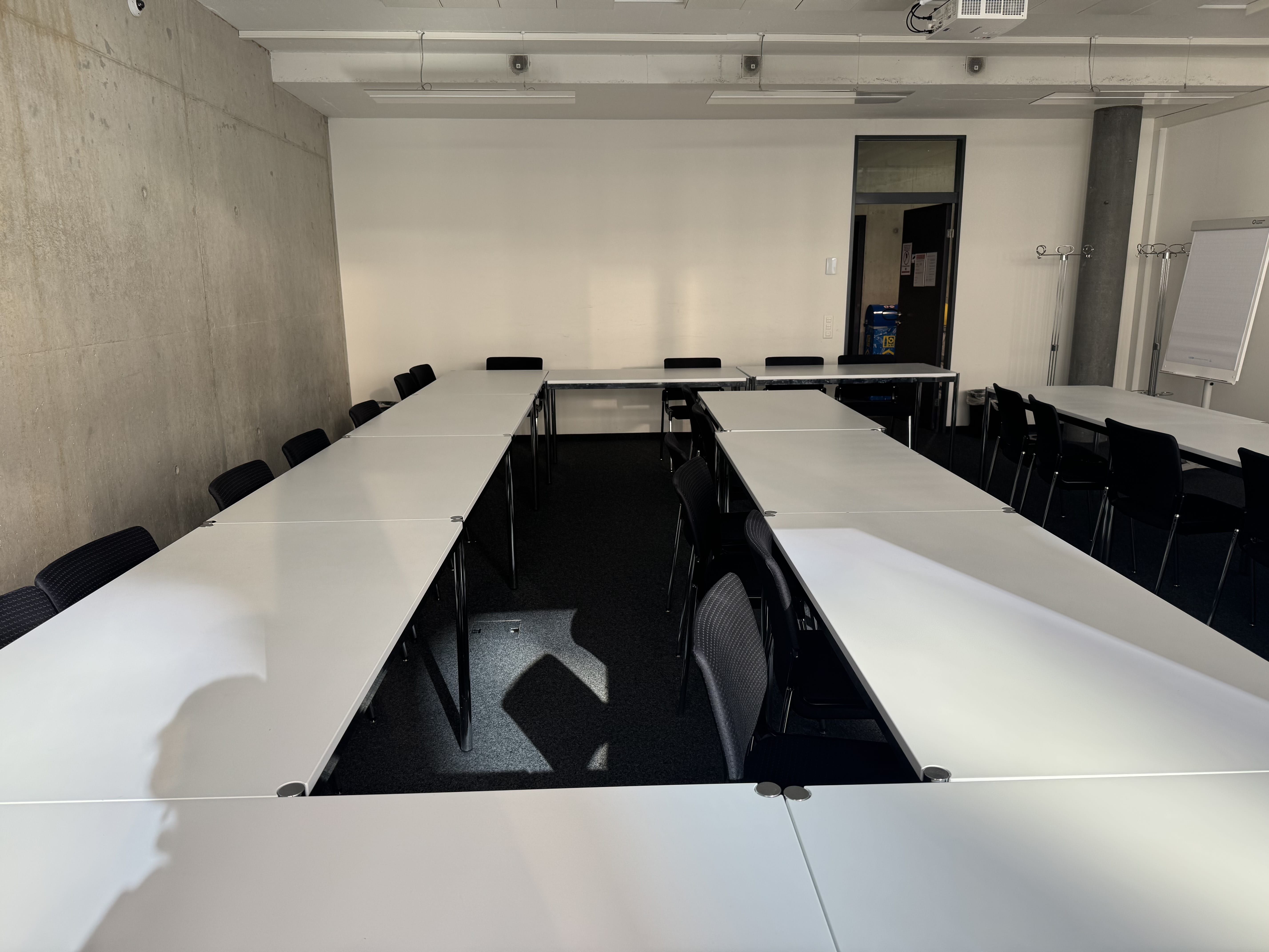 Seminarraum AND-2-06: Ansicht zur Eingangstüre hin. Beengte Stuhlreihe in der Mitte.
