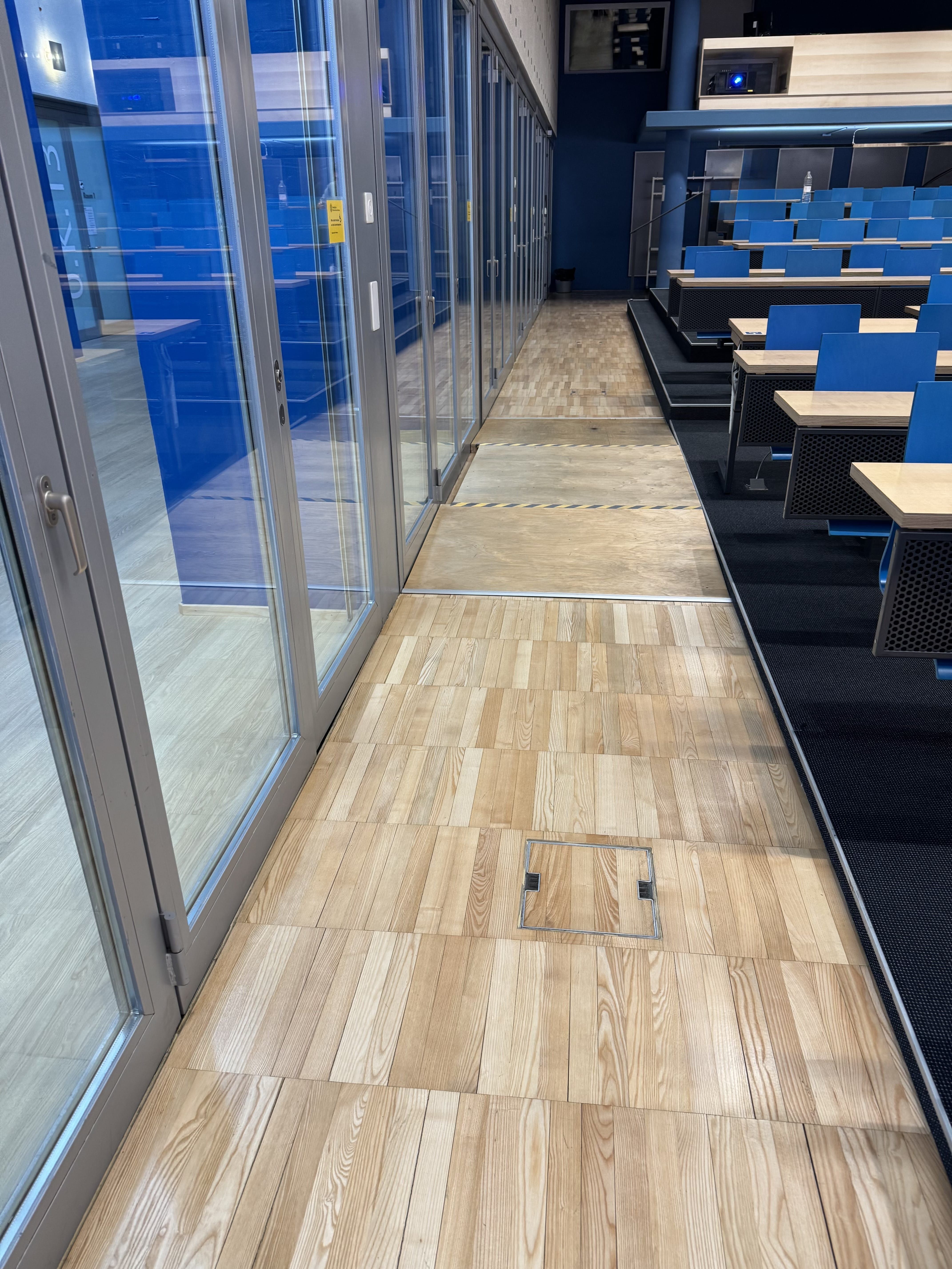 Hörsaal BIN-0-K.02: Ansicht auf die Rampe vor der mittleren Eingangstüre. Gleich rechts davon befindet sich der Tisch mit Rollstuhl-Signet.