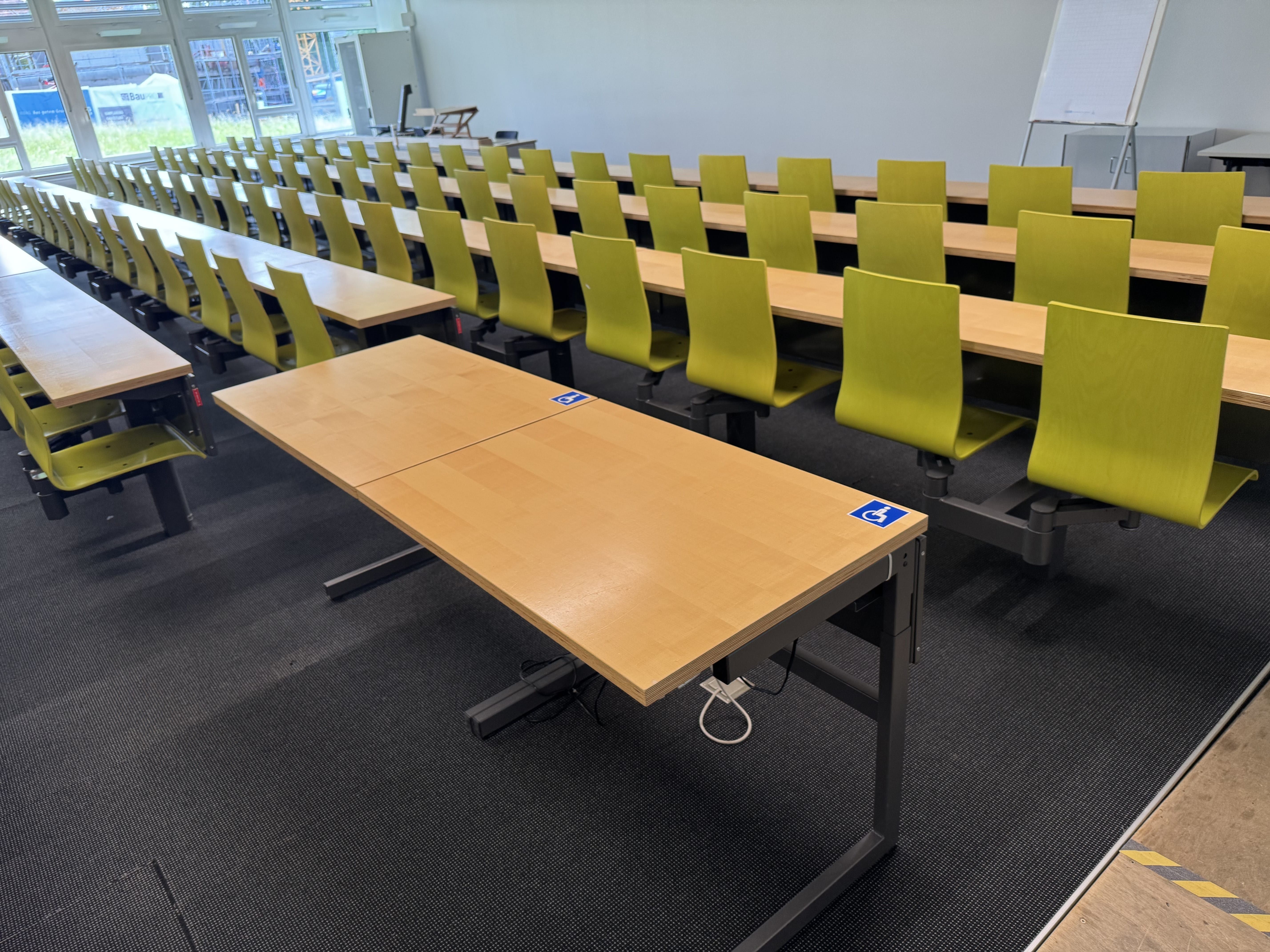 Hörsaal BIN-1-B.01: Ansicht auf die zwei Tische mit Rollstuhl-Signet, die sich neben der Rampe befinden.