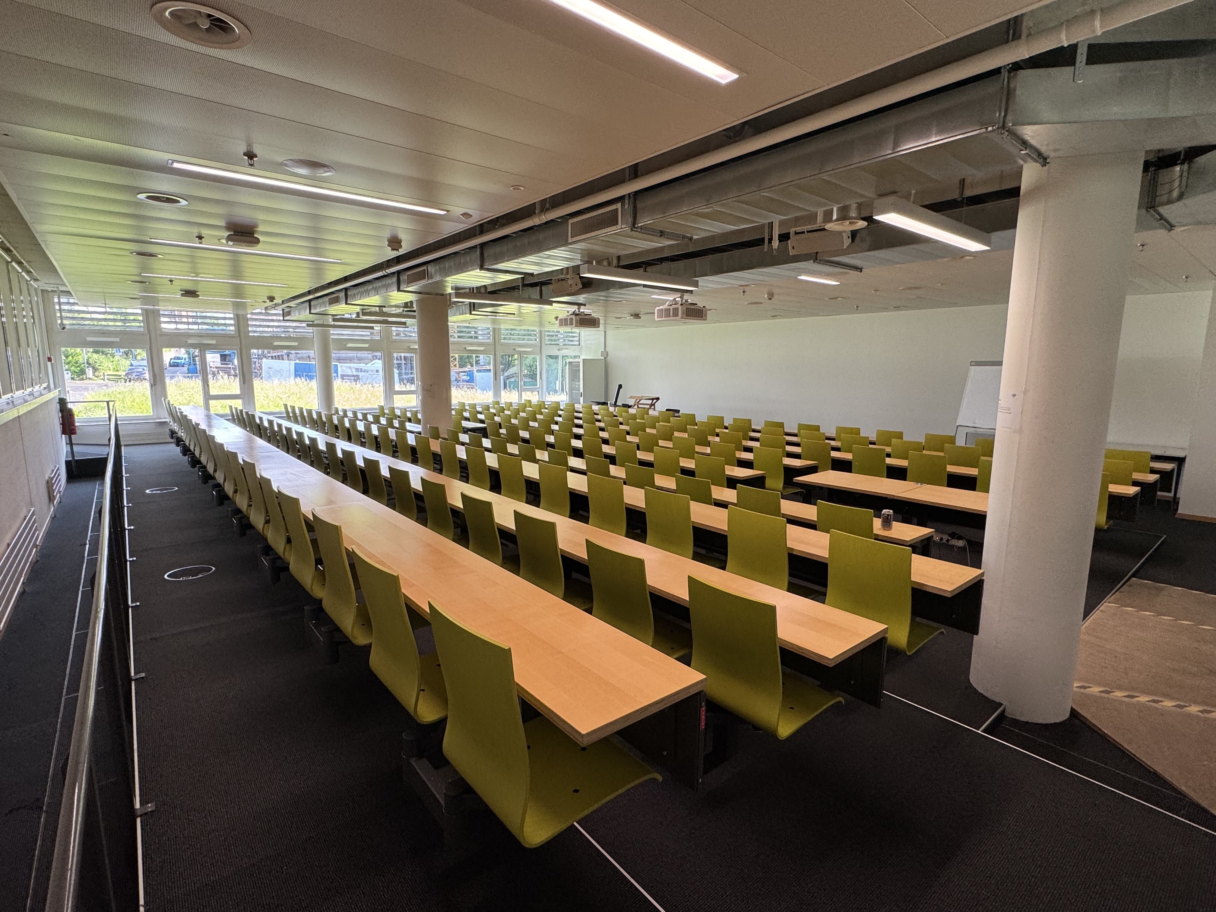 Hörsaal BIN-1-B.01: Ansicht auf den Raum von der hintersten Reihe aus. Alle Sitzreihen sind über eine Stufe oder Schwelle erreichbar mit Ausnahme der zwei Tische für Rollstühle.