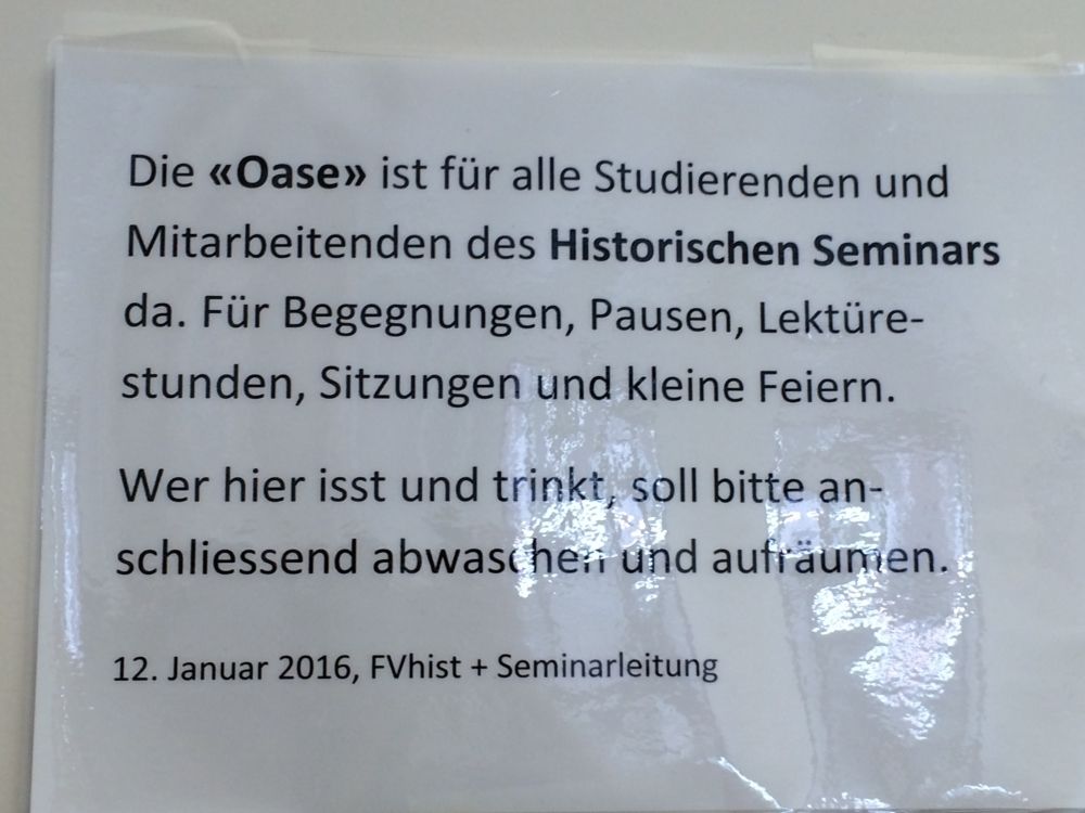 Aufenthaltsraum KO2-G-289a: Hinweistafel auf der Eingangstüre mit folgendem Text:
"Die Oase ist für alle Studierenden und Mitarbeitenden des Historischen Seminars da. Für Begegnungen, Pausen, Lektürestunden, Sitzungen und kleine Feiern. Wer hier isst und trinkt, soll bitte anschliessend abwaschen und aufräumen.