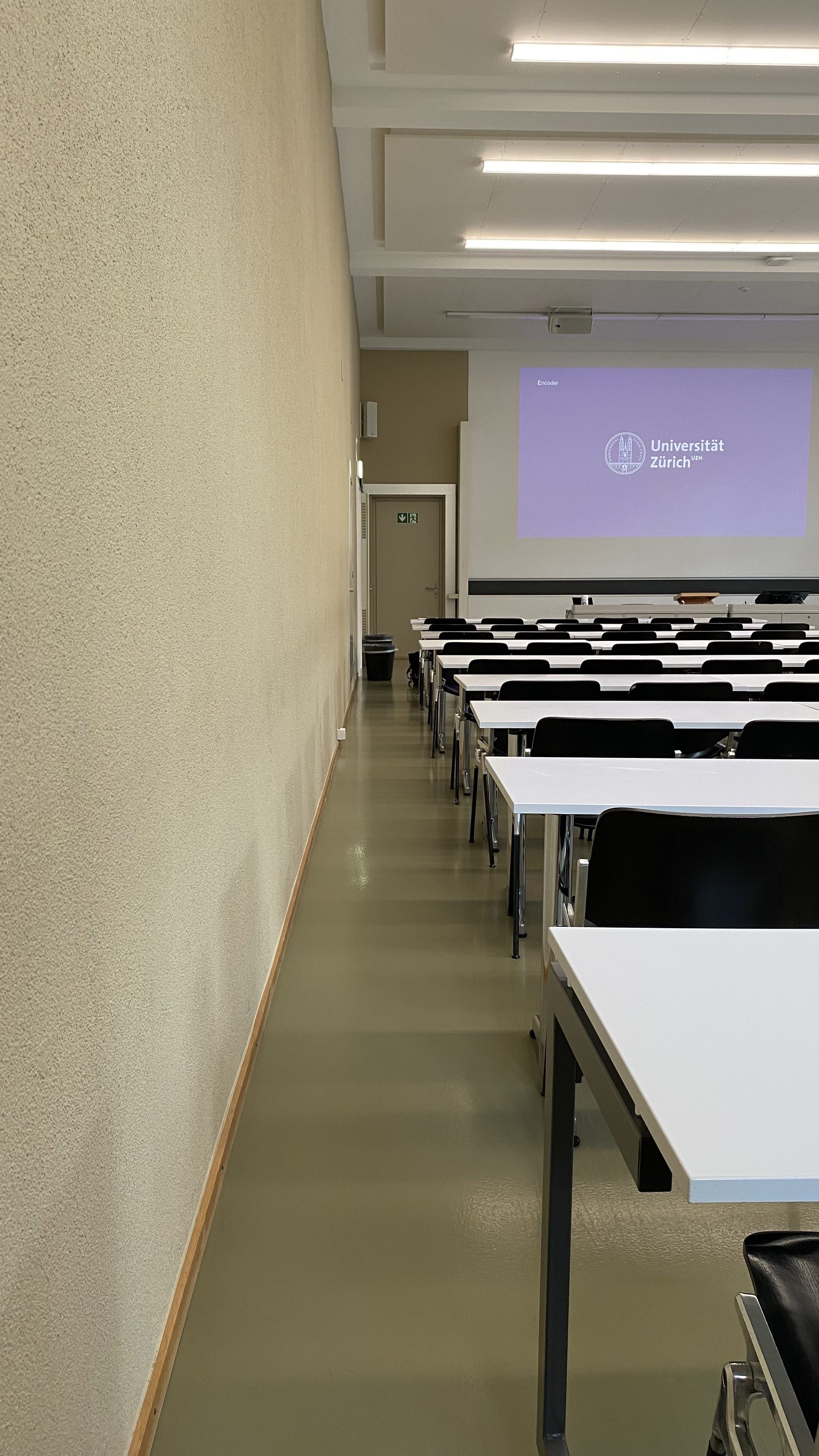 Seminarraum KO2-F-152: Ansicht auf den etwas schmalen Durchgang auf der linken Seite des Raumes zur Eingangstüre hin.