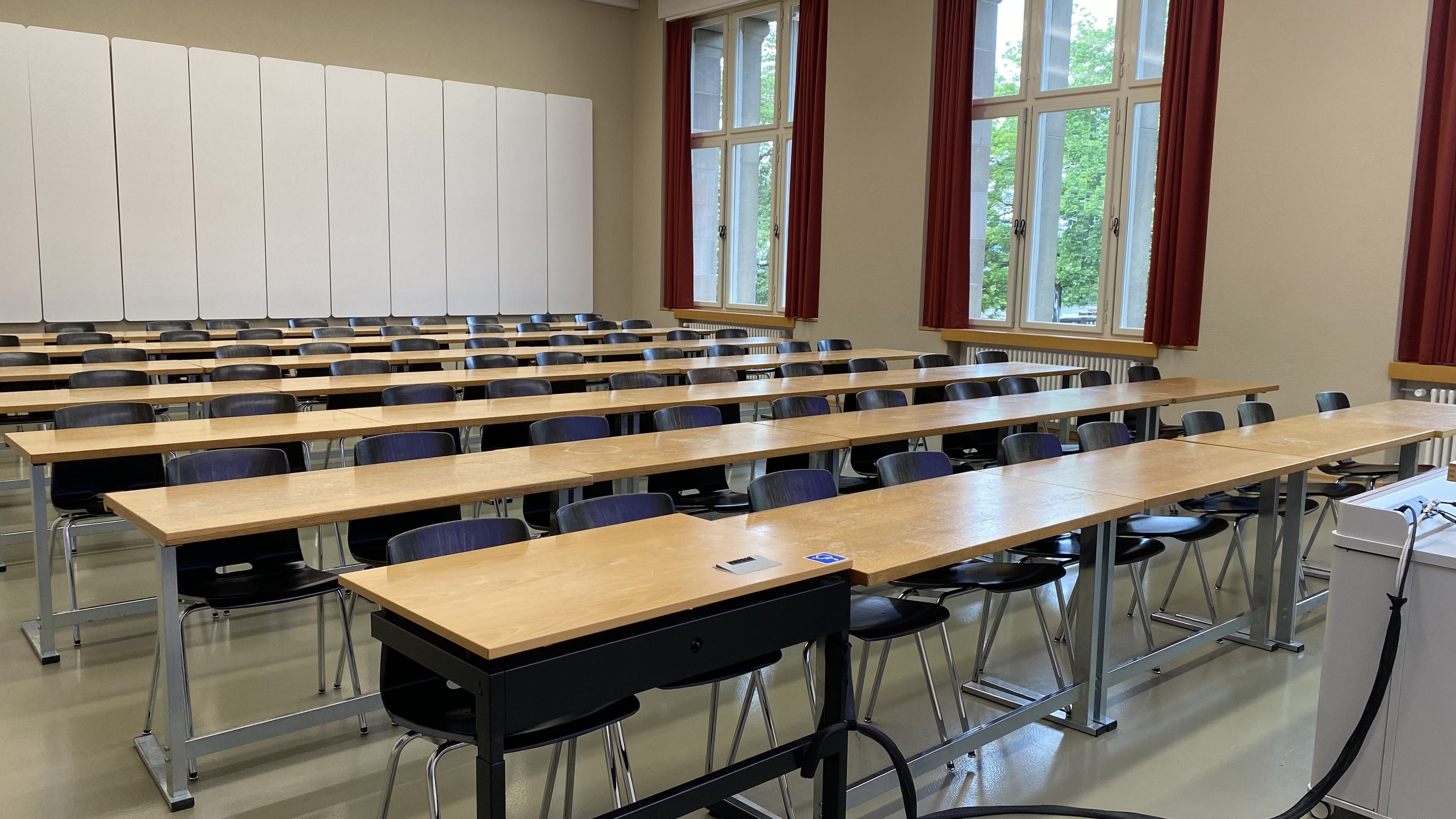 Seminarraum KO2-F-175: Ansicht auf den Raum von der Eingangstüre aus. Ein elektrisch höhenverstellbarer Tisch mit Rollstuhl-Signet befindet sich in der ersten Reihe.