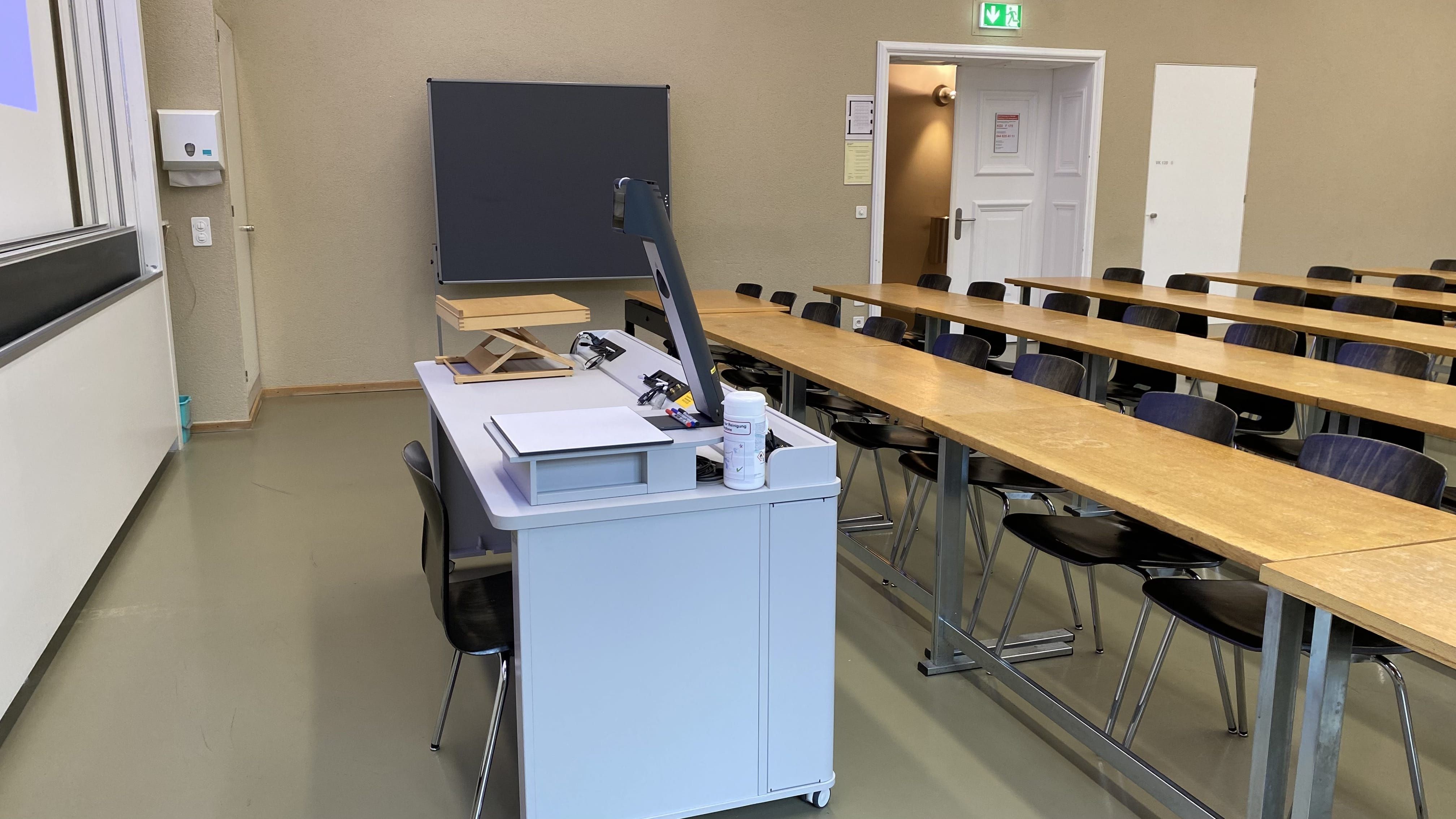 Seminarraum KO2-F-175: Ansicht auf das Dozierendenpult. Die Eingangstüre befindet sich auf der rechten Seite des Bildes.