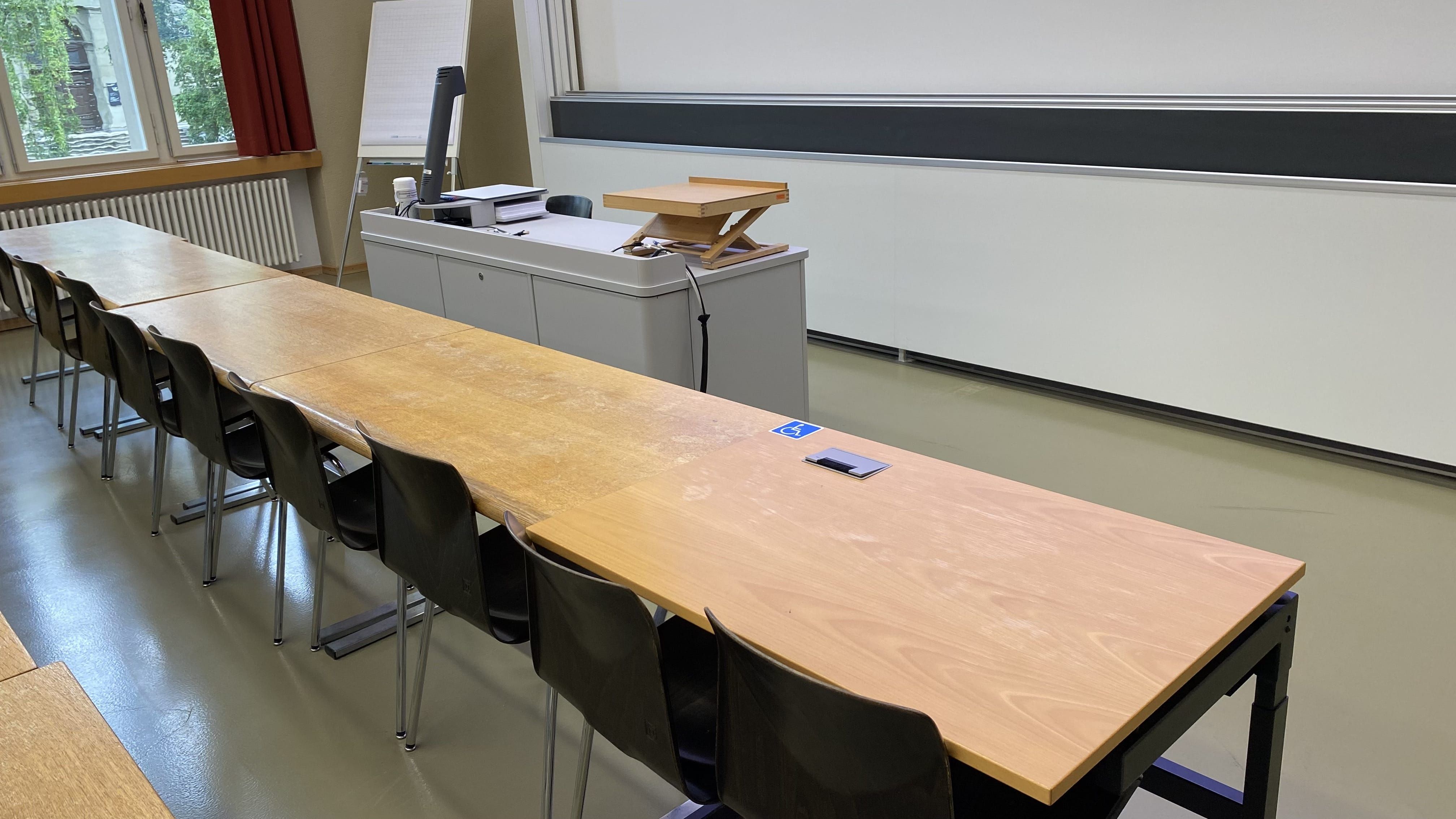Seminarraum KO2-F-175: Ansicht auf den elektrisch höhenverstellbaren Tisch mit Rollstuhl-Signet zum Dozierendenpult hin.