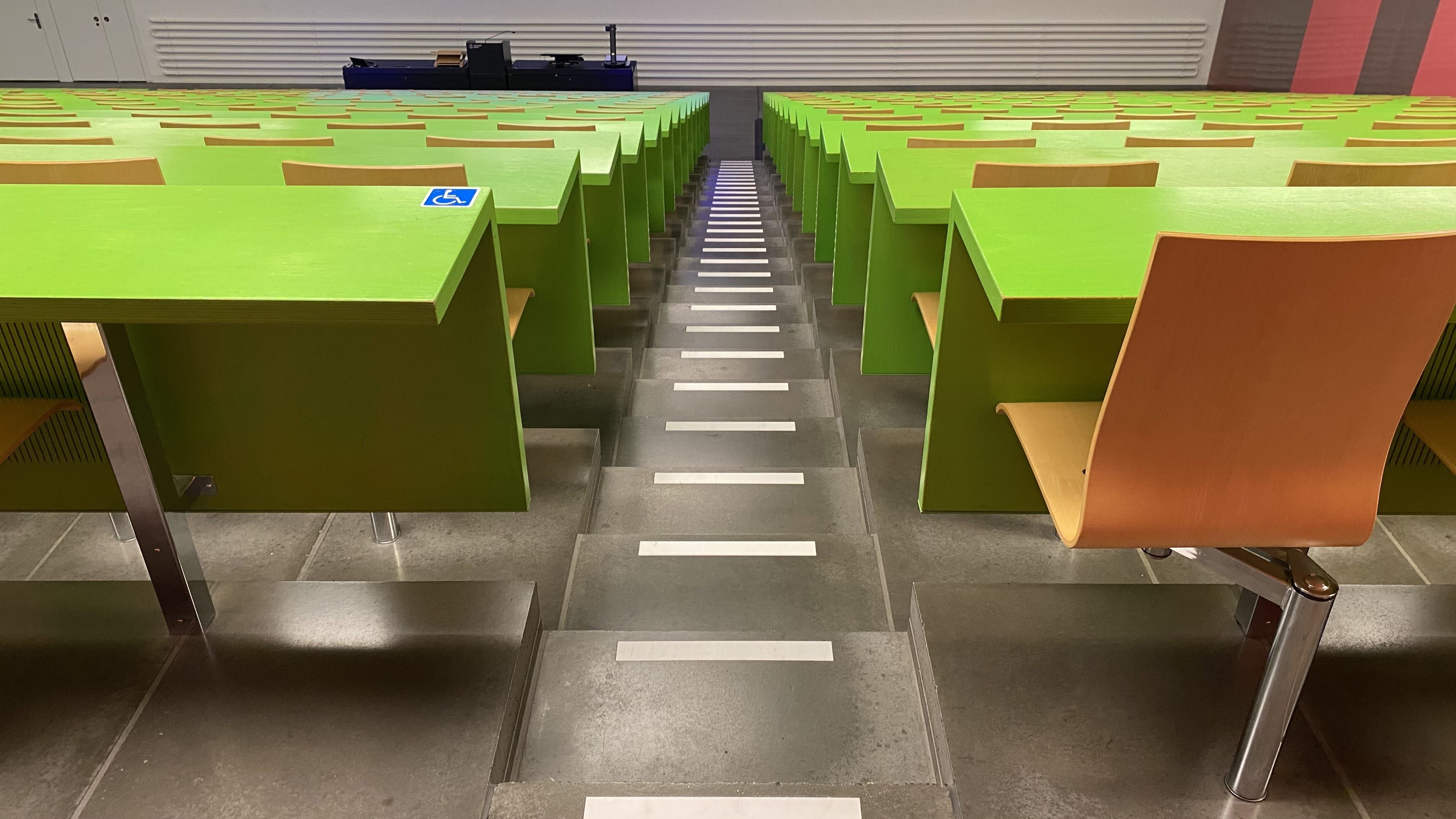 Hörsaal KOH-B-10: Ansicht auf den dritten Tisch mit Rollstuhl-Signet ohne fixe Bestuhlung. Dieser Tisch befindet sich ganz rechts im mittleren Segment der hintersten Reihe.