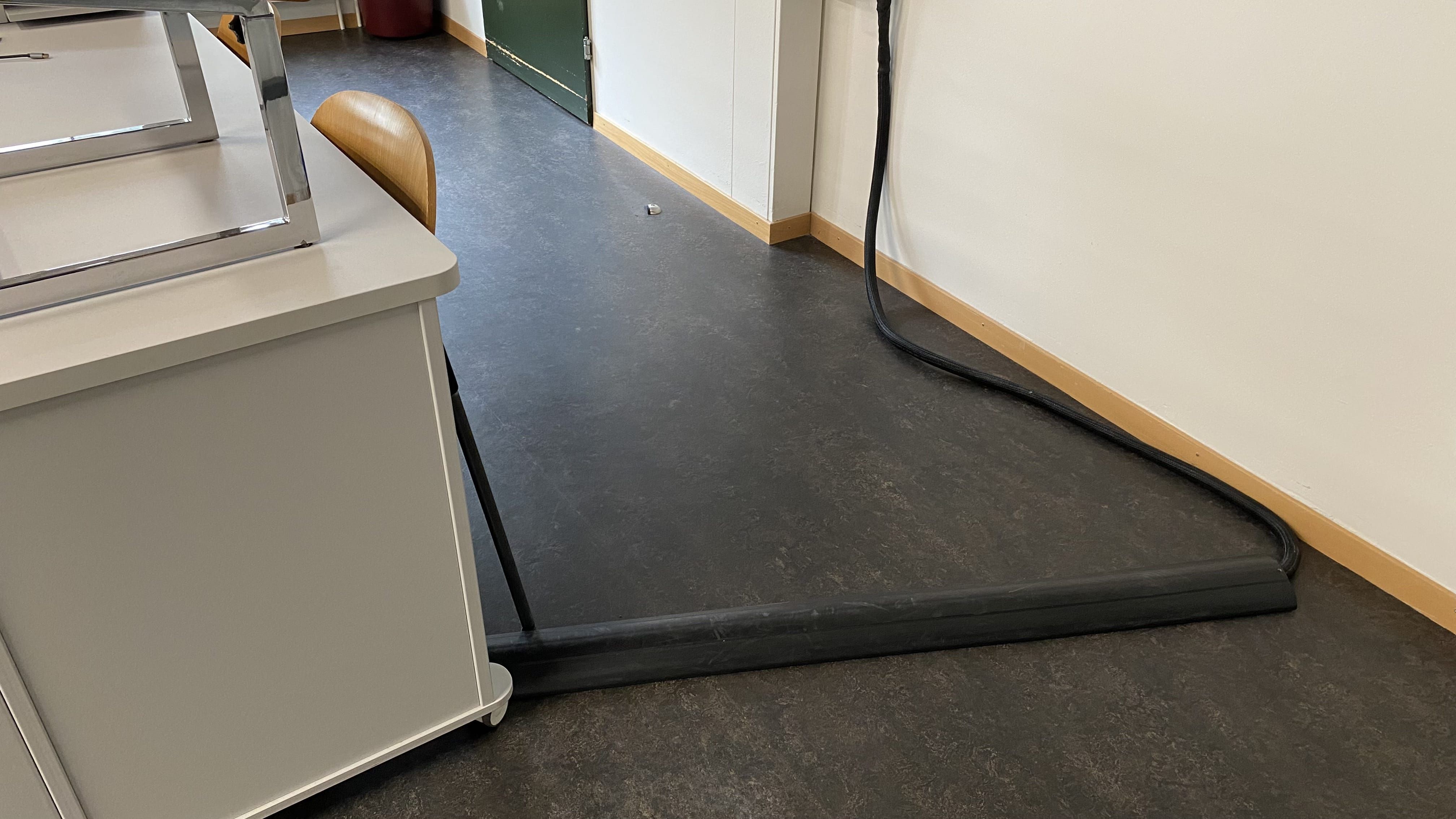 Seminarraum KIR-1-103: Nahansicht auf das Dozierendenpult. Links vom Pult befindet sich eine Kabelschwelle.