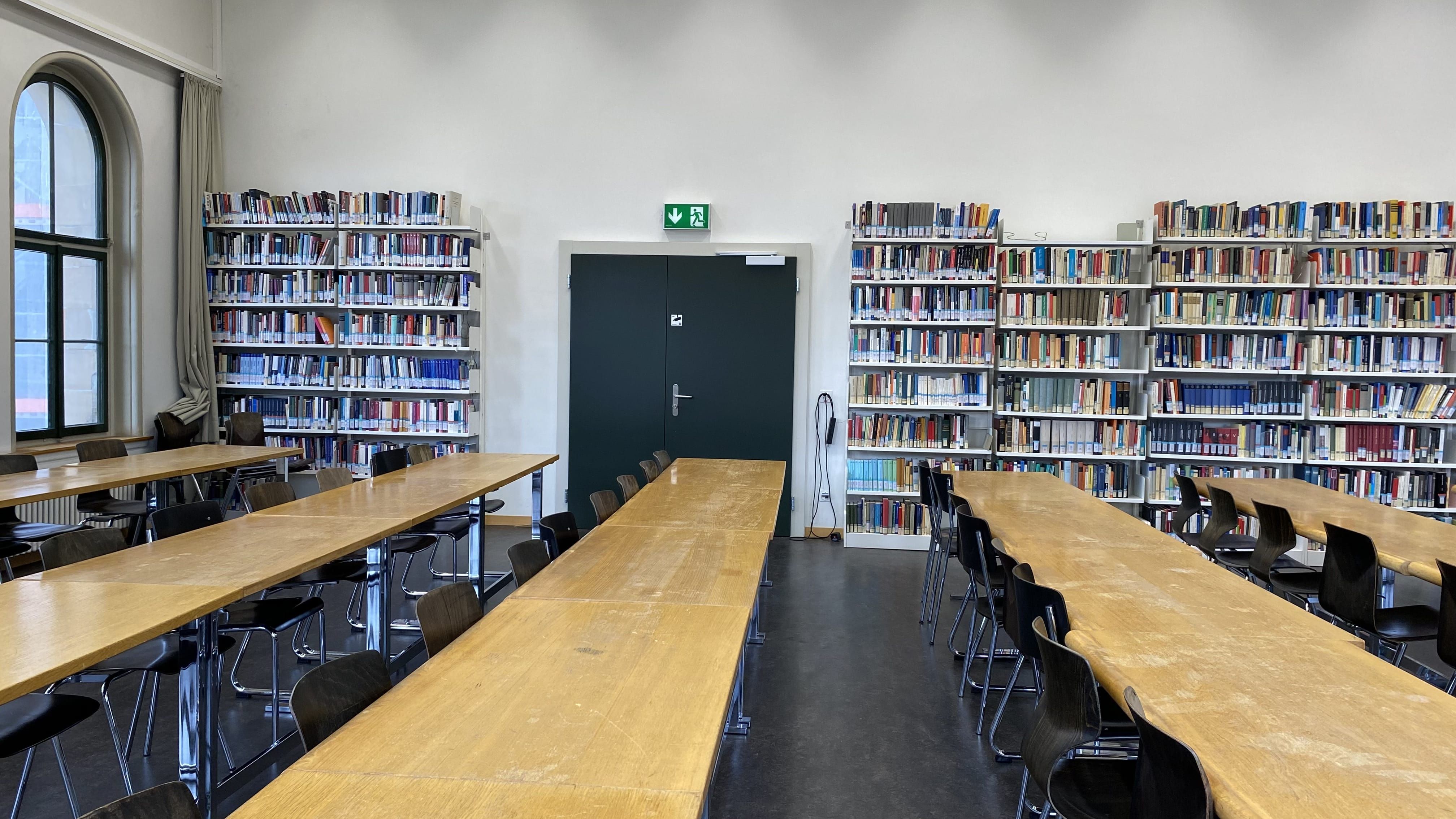 Seminarraum KIR-2-200: Ansicht auf die Bücherwand und die hintere Eingangstüre, entfernt vom Dozierendenpult.