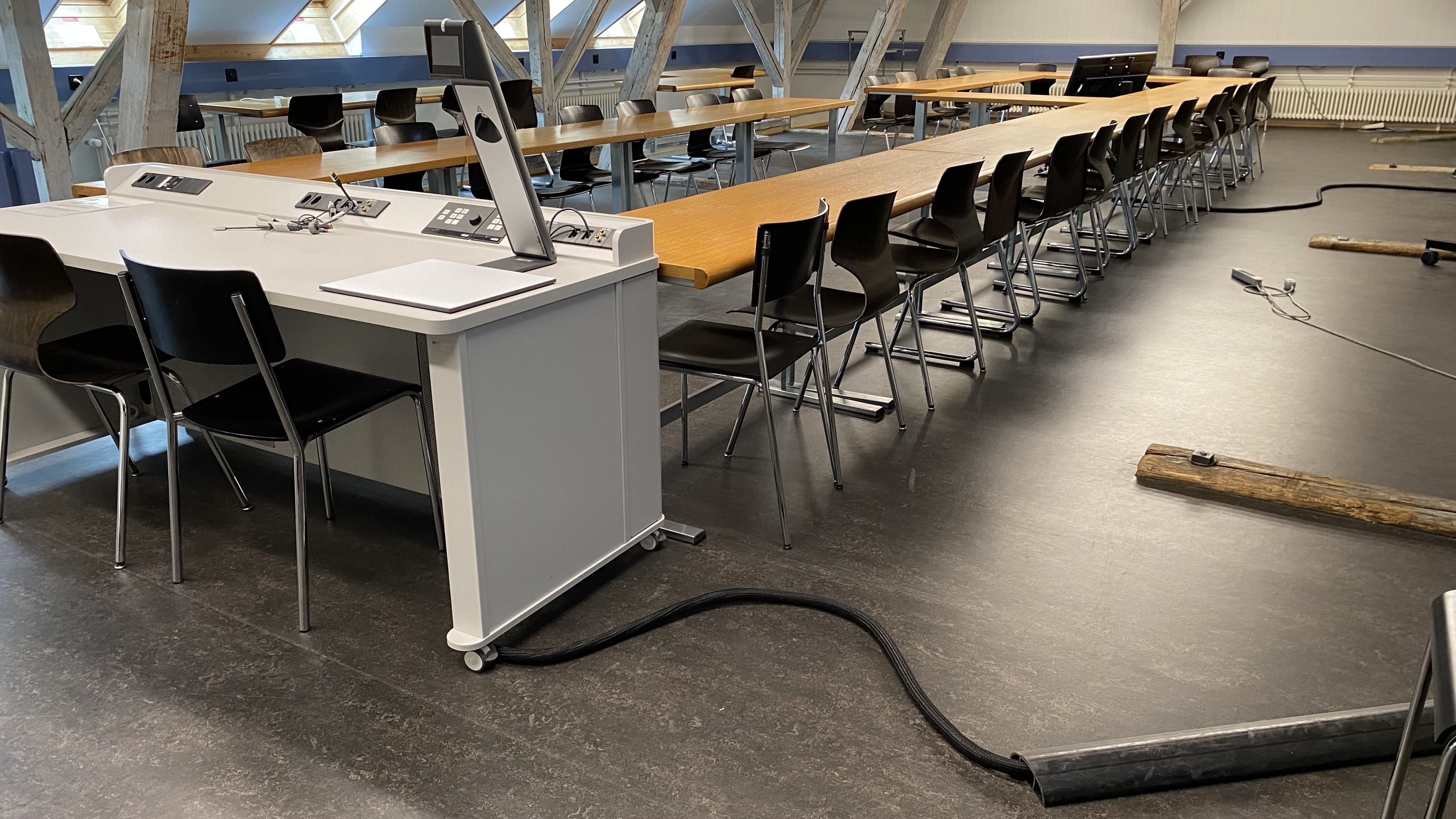 Seminarraum KIR-3-308: Ansicht auf das Dozierendenpult. Rechts vom Pult eine Kabelschwelle.