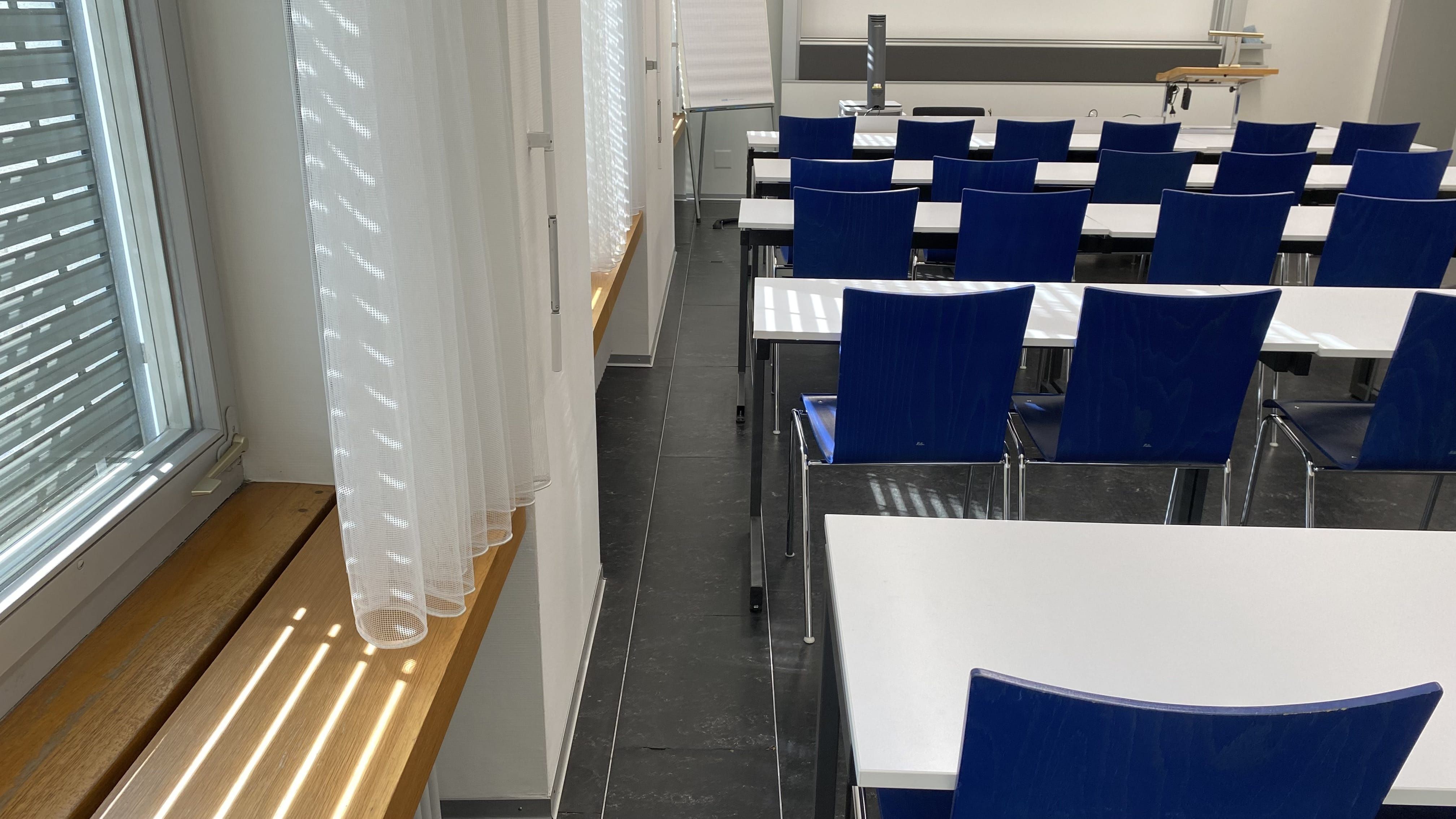 Seminarraum PLD-E-04: Ansicht auf den schmalen Durchgang auf der linken Seite des Raumes zum Dozierendenpult hin.