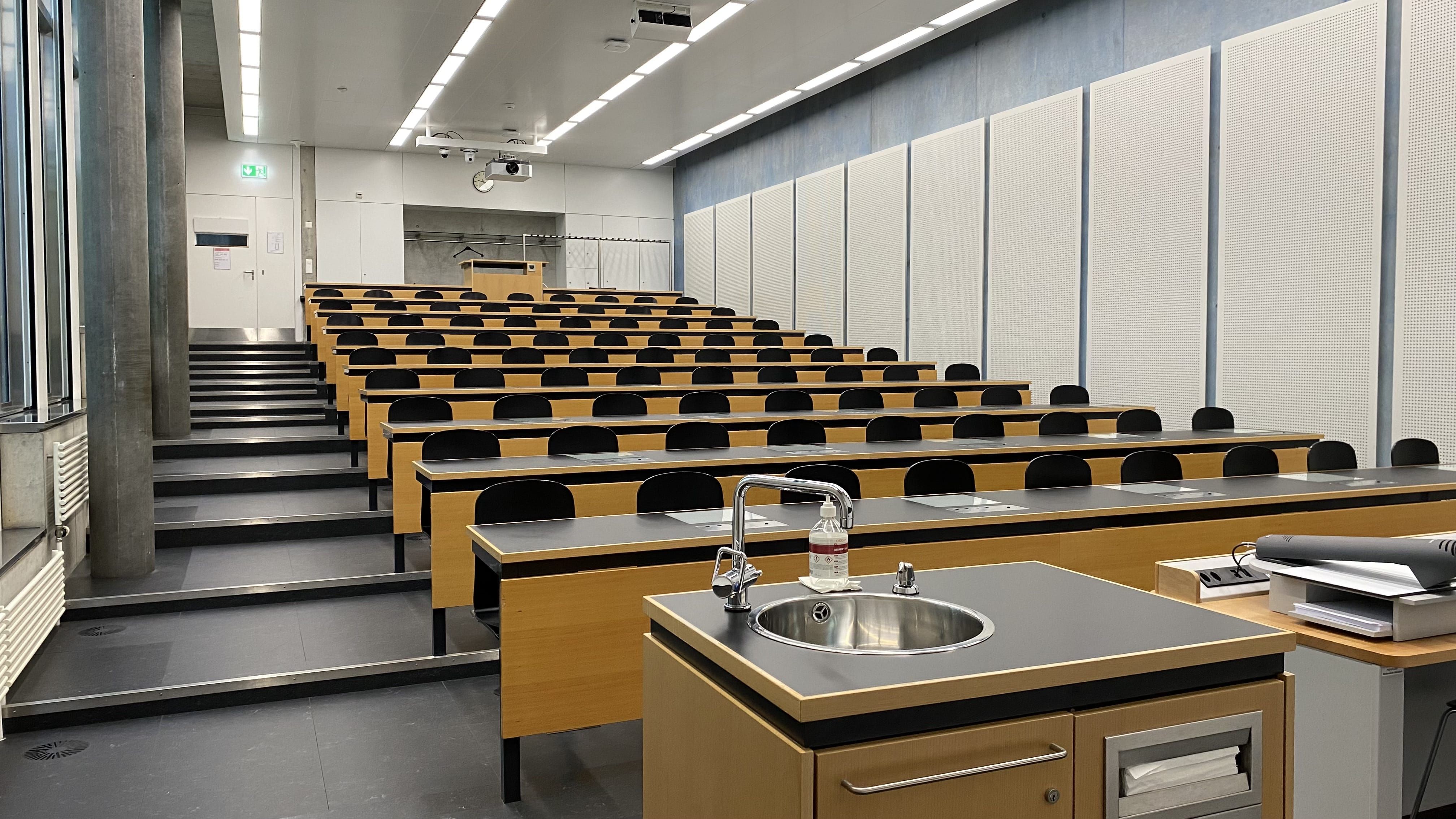 Hörsaal PLF-U1-205: Ansicht auf den Raum vom Dozierendenpult aus. Die Eingangstüre befindet sich links oberhalb der Stufen im Bild.