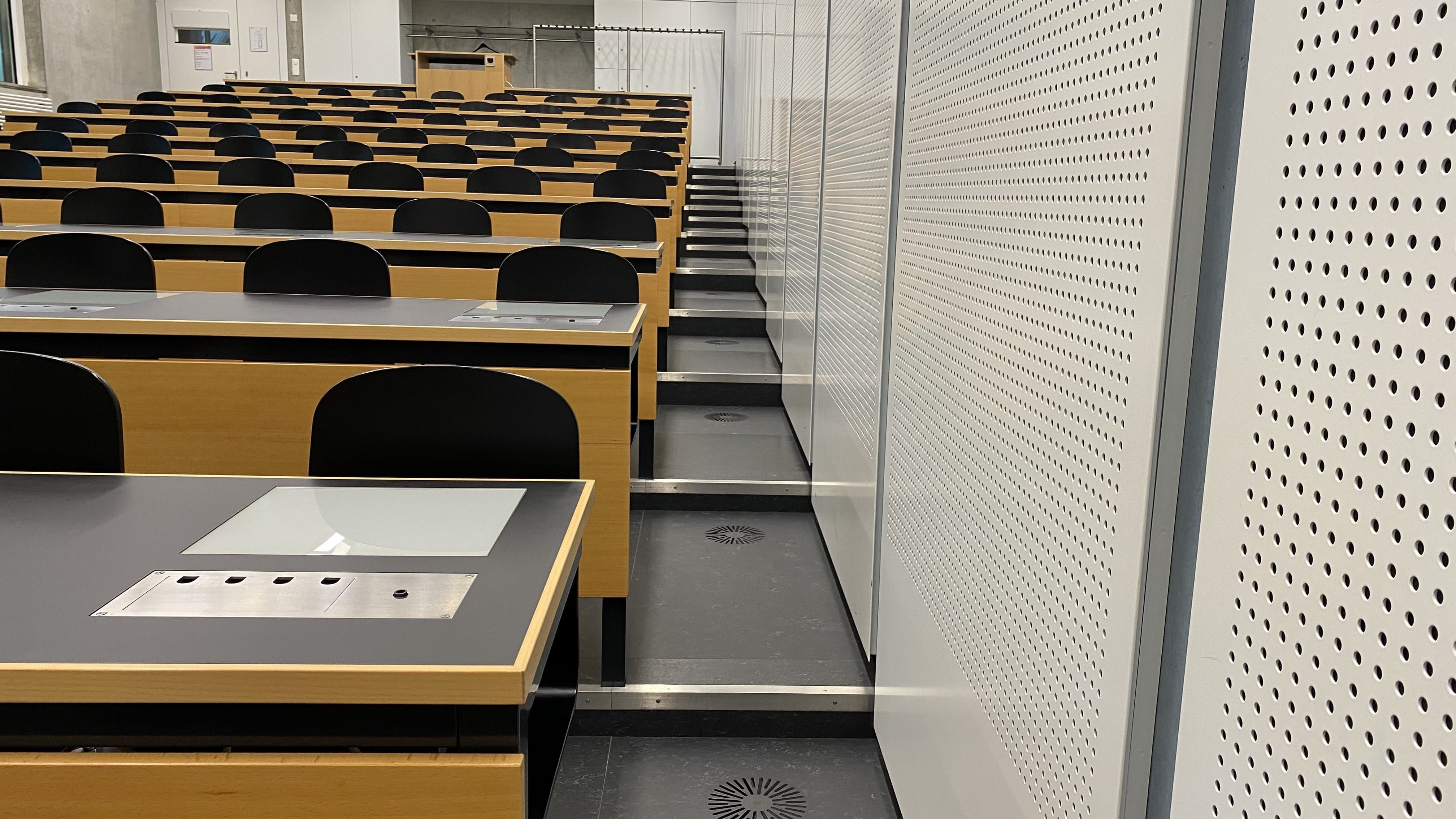 Hörsaal PLF-U1-205: Ansicht auf die Treppen auf der rechten Seite des Raumes vom Dozierendenpult aus. Der Durchgang ist schmal.