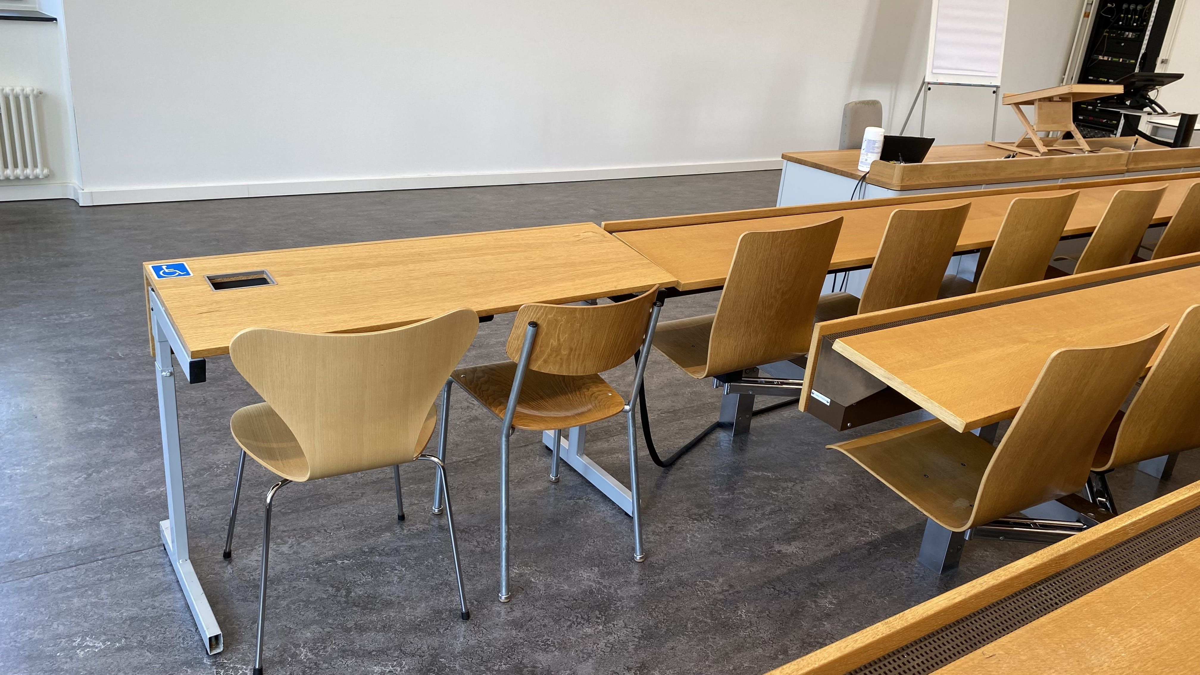 Seminarraum RAI-G-41: Ansicht auf den zweiten Tisch mit Rollstuhl-Signet ohne fixe Bestuhlung in der ersten Reihe. Dieser Tisch befindet sich auf der linken Seite des Raumes.