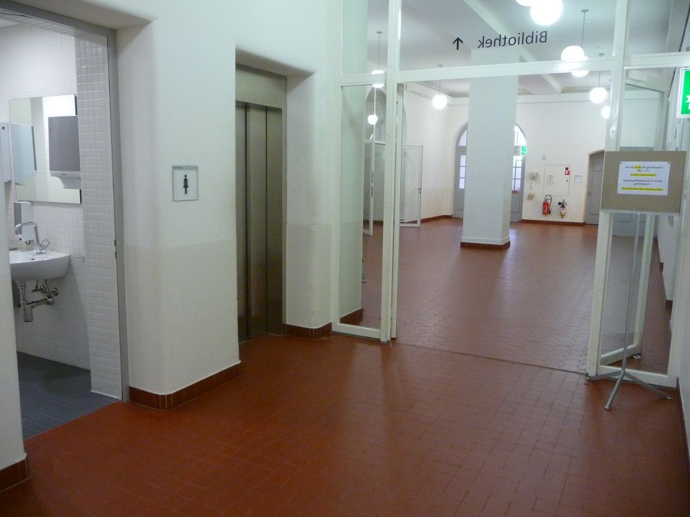 RAI, Lift A bei der Cafeteria, für Rollstuhlbenutzende.: Links neben dem Lift befinden sich WC`s. Geht man durch die Glastür in den Eingangsbereich des Gebäudes, liegt die Cafeteria auf der rechten Seite, links befindet sich das Treppenhaus.