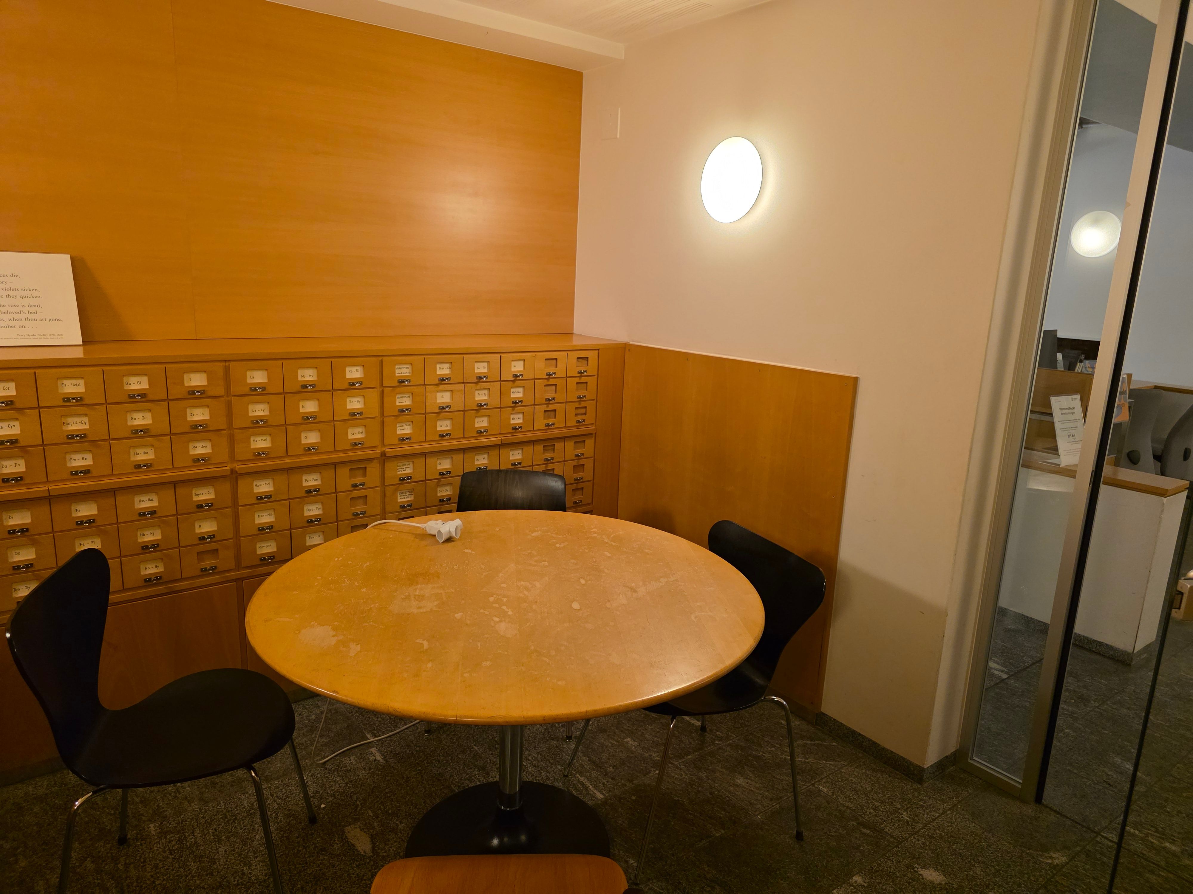PET-1-4E: Geschlossener Lernraum. Blick des Raums von der gegenüberliegenden Seite vom Eingang aus. Vier Stühle stehen um einen runden Tisch herum.