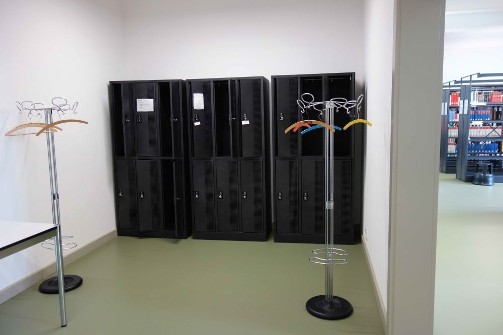 RAA-F, Schliessfächer/Garderobe: Die Schliessfächer und Garderobenständer im Raum F-02. Links im Bild ist der Tisch zu erkennen. Rechts im Bild ist der Übergang zum Raum F-01 zu sehen.
