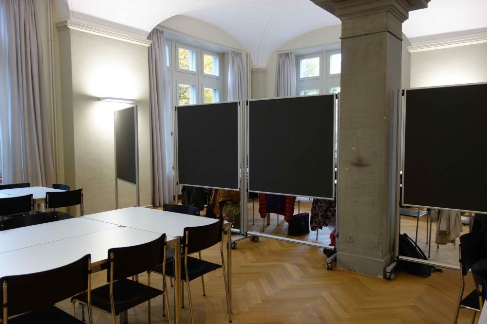 Seminarraum RAA-E-30: Der hintere Teil des Workshopraums. Links im Bild sind die Gruppenarbeitsplätze zu sehen, in der Mitte/rechts die verschiebbaren Whiteboard-/Wandtafeln und die Säule.