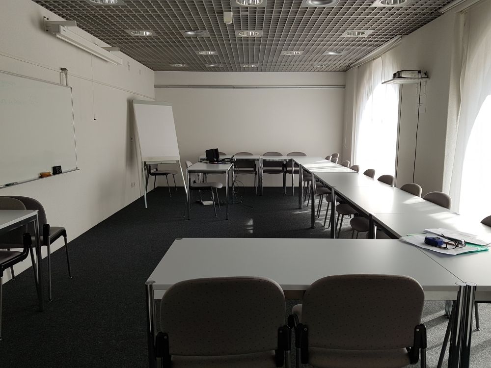 Seminarraum UNK-E-2: Der Seminarraum von der Türe aus gesehen. Die Tische sind U-förmig um den Raum verteilt. Die Wandtafel befindet sich hier auf der linken Seite. Die Bestuhlung ist nicht fix und die Tische können verschoben werden.