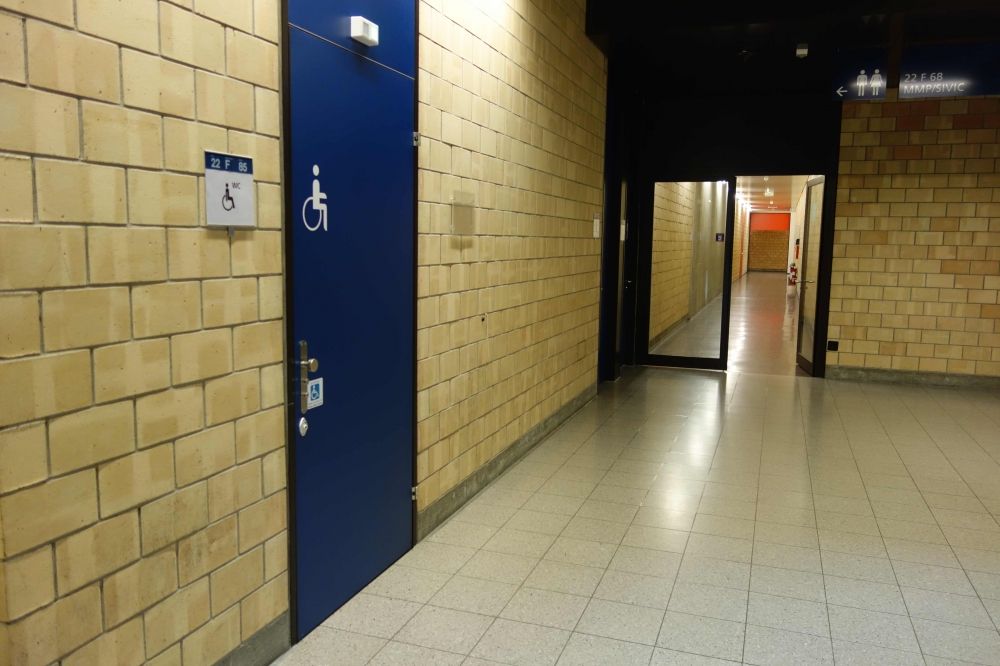 Y21, Stockwerk F: Gerade auf der Rückseite des Lifts des Y21 befindet sich ein Rollstuhl-WC. Kommt man vom Lift her und geht zu diesem WC, so führt in genau dieser Richtung geradeaus ein langer Gang ins Y22 (siehe Foto). Am Ende des Ganges links abzweigen. Den Gang dort entlang bis in den offenen Bereich (Halle) des Y04.
