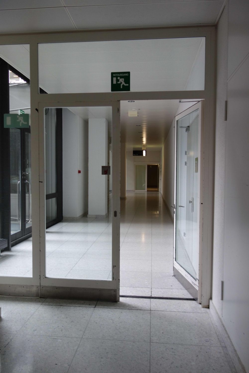 Hörsaal Y35-F-32: Stufenloser Zugang zum Hörsaal: Blick vom Lift des Gebäudes Y34 Richtung links zum Gebäude Y15. Der Weg zum Hörsaal führt durch die erste Glastür und biegt beim Schild vor der zweiten, im Bild hinten erkennbaren Tür links ab.
