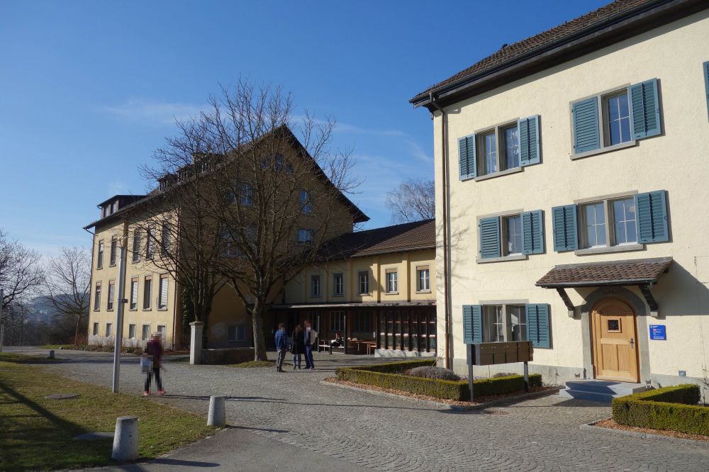 Gebäude Y63: Aussensicht auf das Gebäude und den Vorplatz.
                            Rechts der Ostflügel, links der Westflügel und in der Mitte der
                            Zwischentrakt, wo sich der Haupteingang befindet (nicht auf dem Bild).