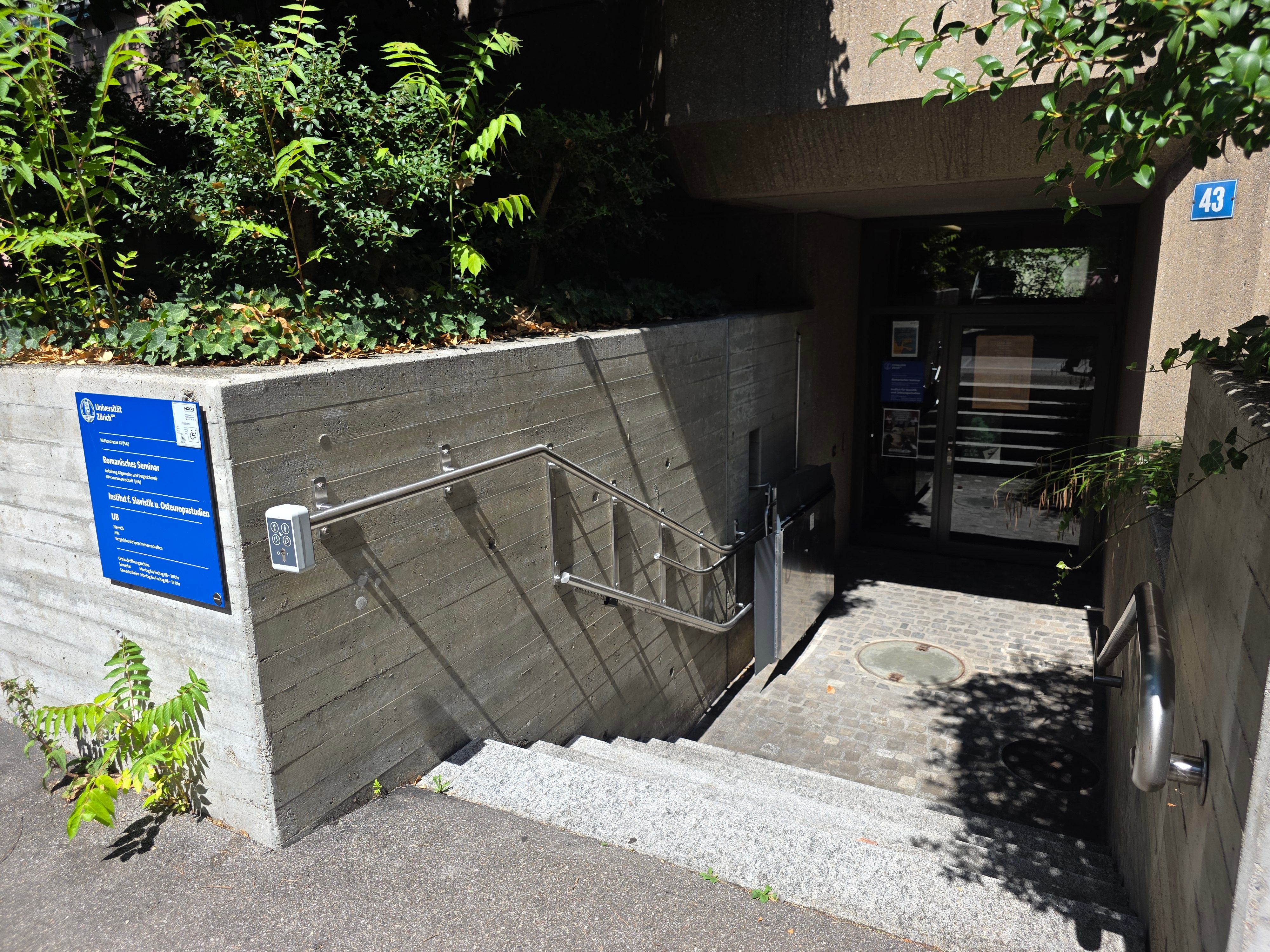 PLG Gebäude: Auf dem Bild sieht man die Stufen zum Haupteingang und den Treppenlift, der einen stufenlosen Zugang ins Stockwerk A / 1. UG ermöglicht.