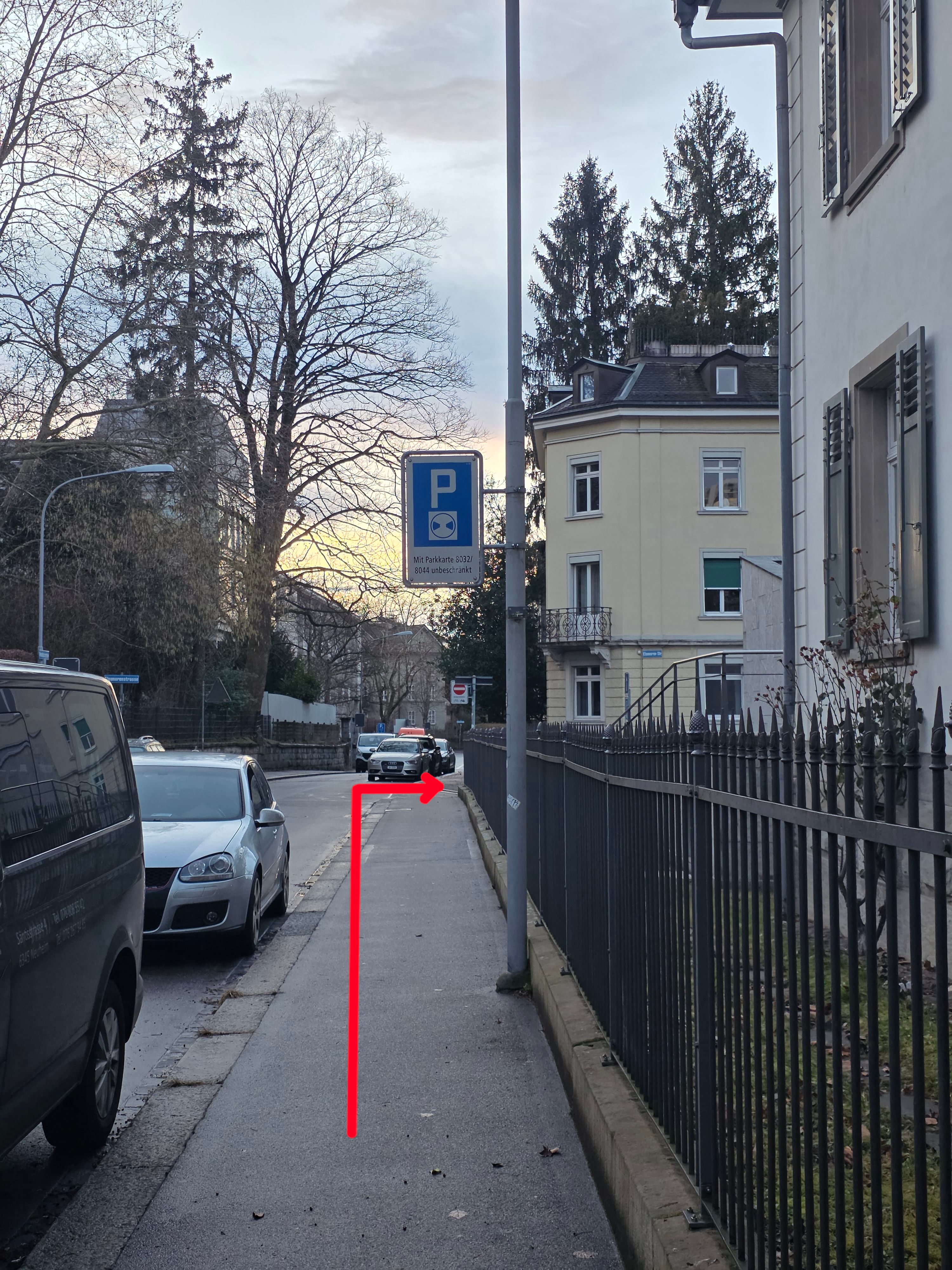 PET Gebäude: Der Weg zum stufenlosen Eingang ist mit einem roten Pfeil markiert.
1) Vom Haupteingang aus muss man nach links abbiegen und dann am Ende des Trottoirs nach rechts.